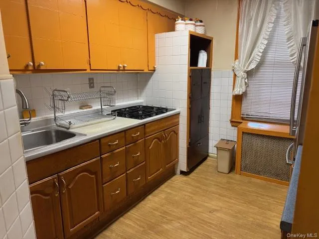 Kitchen featuring light countertops, light wood-style flooring, tile walls, gas stovetop, and radiator Kitchen featuring light countertops, light wood-style flooring, tile walls, gas stovetop, and radiator