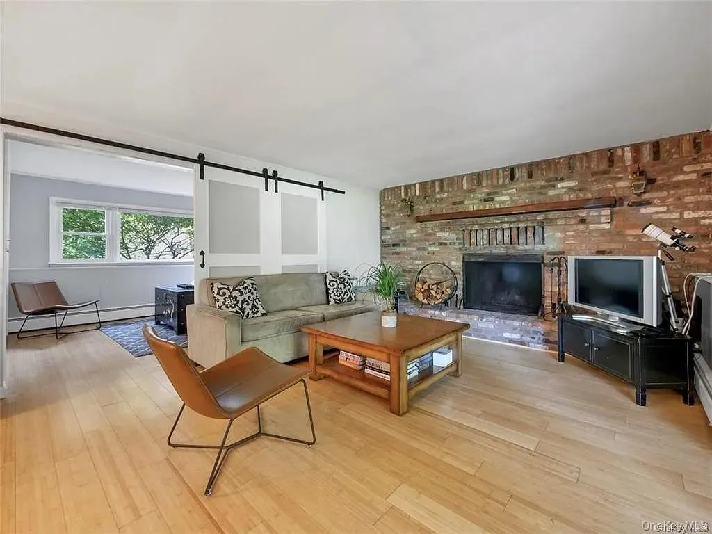 Living room with a brick fireplace, a barn door, light wood-type flooring, brick wall, and a baseboard radiator Living room with a brick fireplace, a barn door, light wood-type flooring, brick wall, and a baseboard radiator