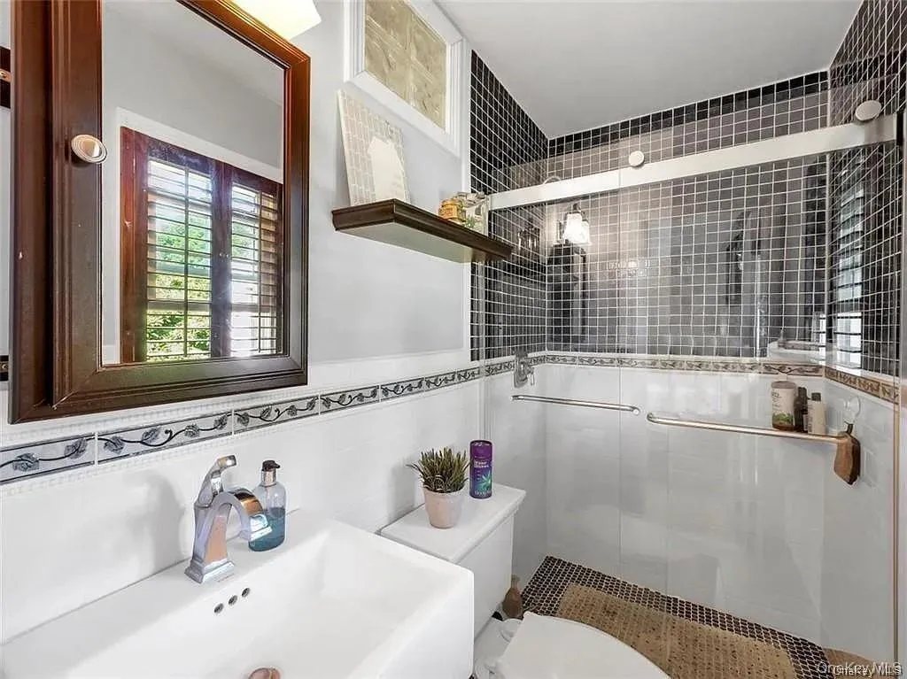 Bathroom featuring tile walls, toilet, sink, and an enclosed shower Bathroom featuring tile walls, toilet, sink, and an enclosed shower