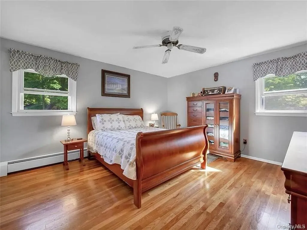 Bedroom with multiple windows, a baseboard radiator, ceiling fan, and light hardwood / wood-style floors Bedroom with multiple windows, a baseboard radiator, ceiling fan, and light hardwood / wood-style floors