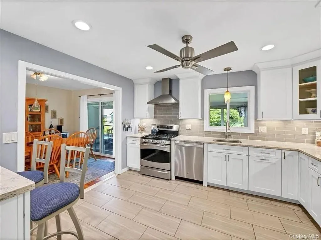 Kitchen with ceiling fan, stainless steel appliances, wall chimney exhaust hood, and a healthy amount of sunlight Kitchen with ceiling fan, stainless steel appliances, wall chimney exhaust hood, and a healthy amount of sunlight