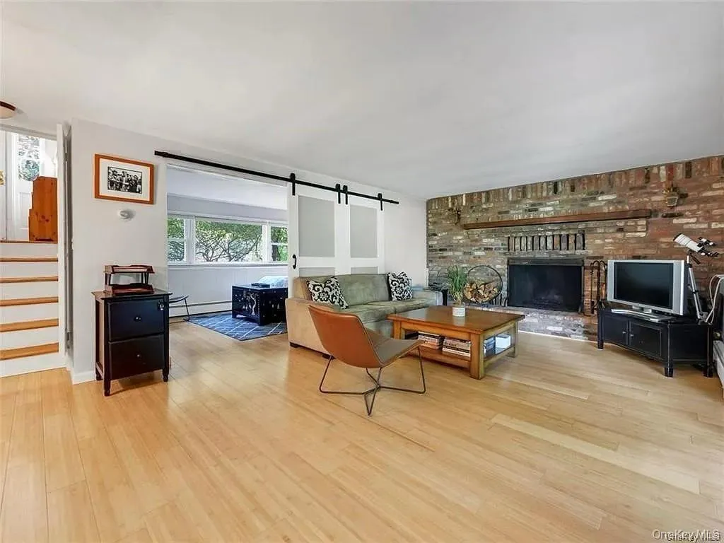 Living room with brick wall, light hardwood / wood-style floors, a brick fireplace, a barn door, and baseboard heating Living room with brick wall, light hardwood / wood-style floors, a brick fireplace, a barn door, and baseboard heating