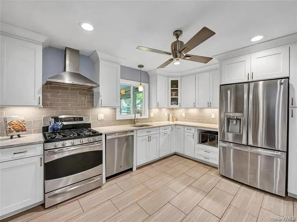 Kitchen featuring wall chimney exhaust hood, appliances with stainless steel finishes, hanging light fixtures, ceiling fan, and white cabinets Kitchen featuring wall chimney exhaust hood, appliances with stainless steel finishes, hanging light fixtures, ceiling fan, and white cabinets