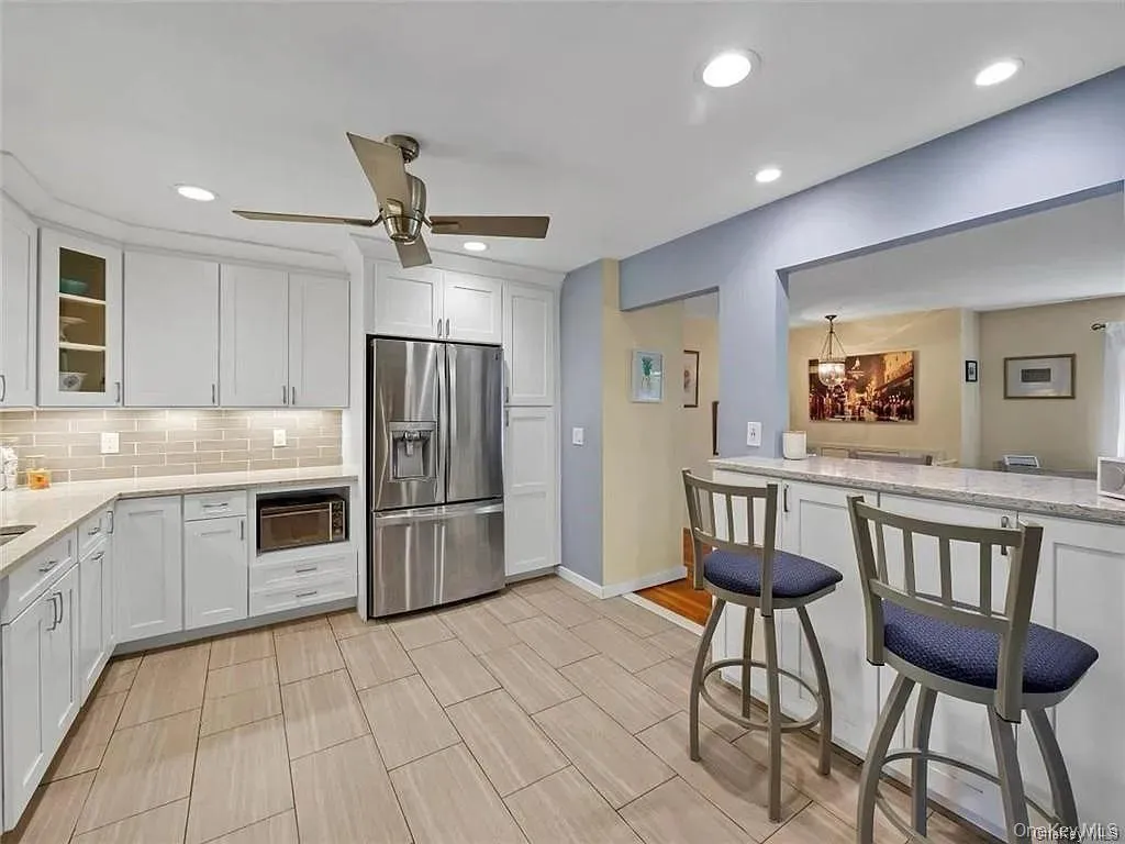 Kitchen featuring backsplash, stainless steel fridge with ice dispenser, kitchen peninsula, white cabinetry, and ceiling fan Kitchen featuring backsplash, stainless steel fridge with ice dispenser, kitchen peninsula, white cabinetry, and ceiling fan