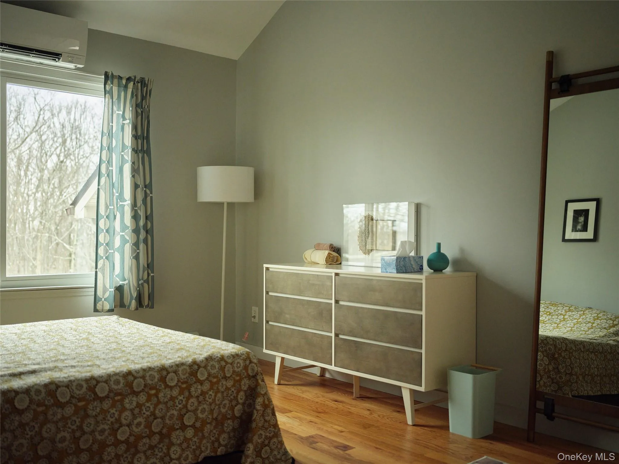 Bedroom with an AC wall unit, light wood finished floors, and vaulted ceiling Bedroom with an AC wall unit, light wood finished floors, and vaulted ceiling
