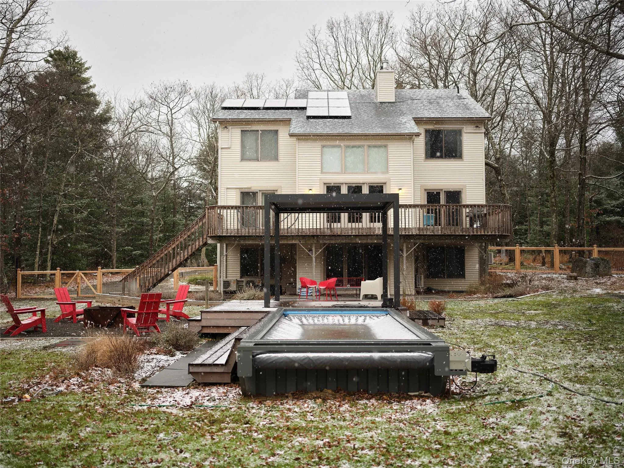 Back of house with a deck, roof mounted solar panels, a fire pit, a chimney, and stairs Back of house with a deck, roof mounted solar panels, a fire pit, a chimney, and stairs