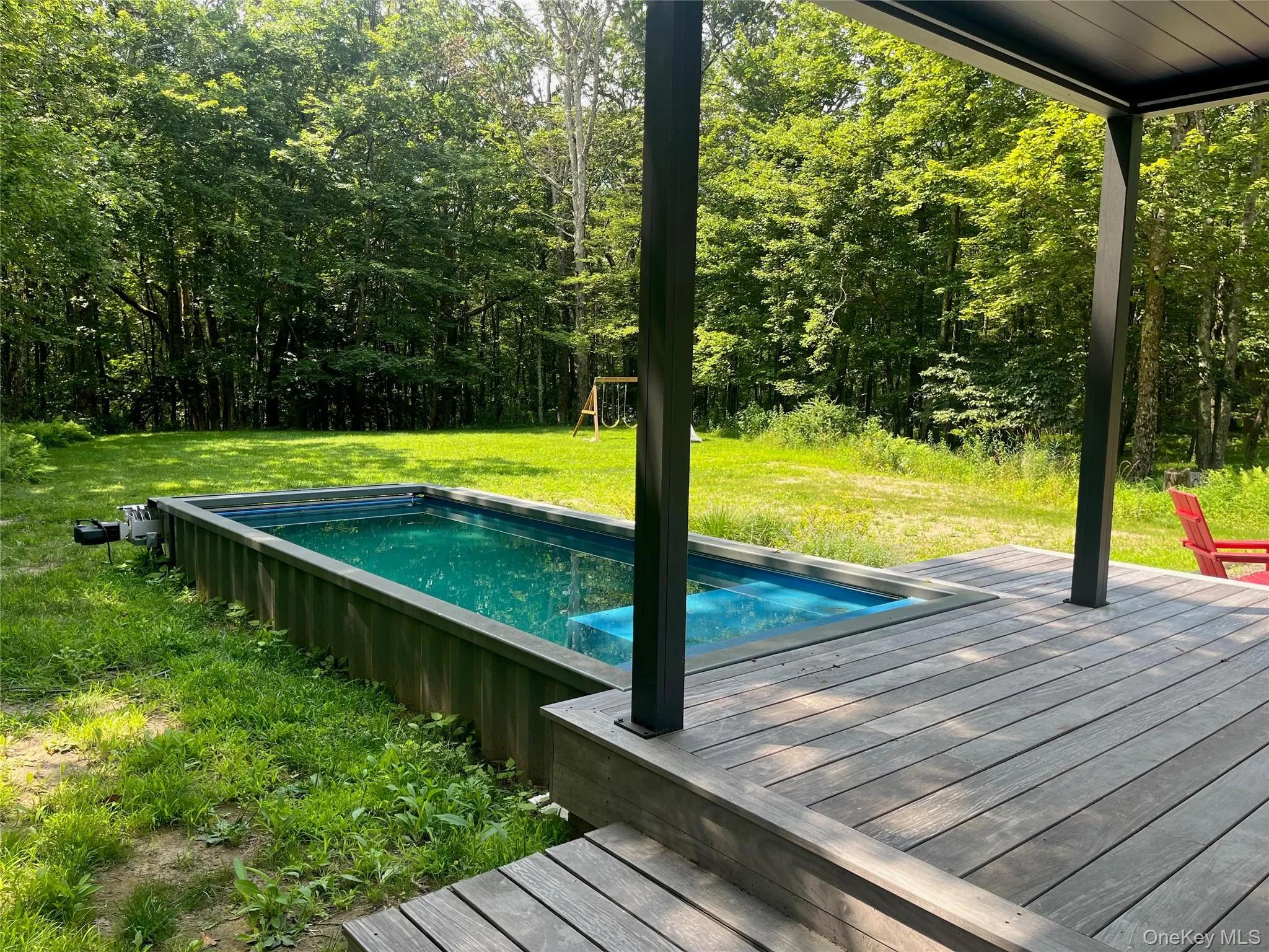 Outdoor pool featuring a lawn, a wooden deck, and a playground Outdoor pool featuring a lawn, a wooden deck, and a playground