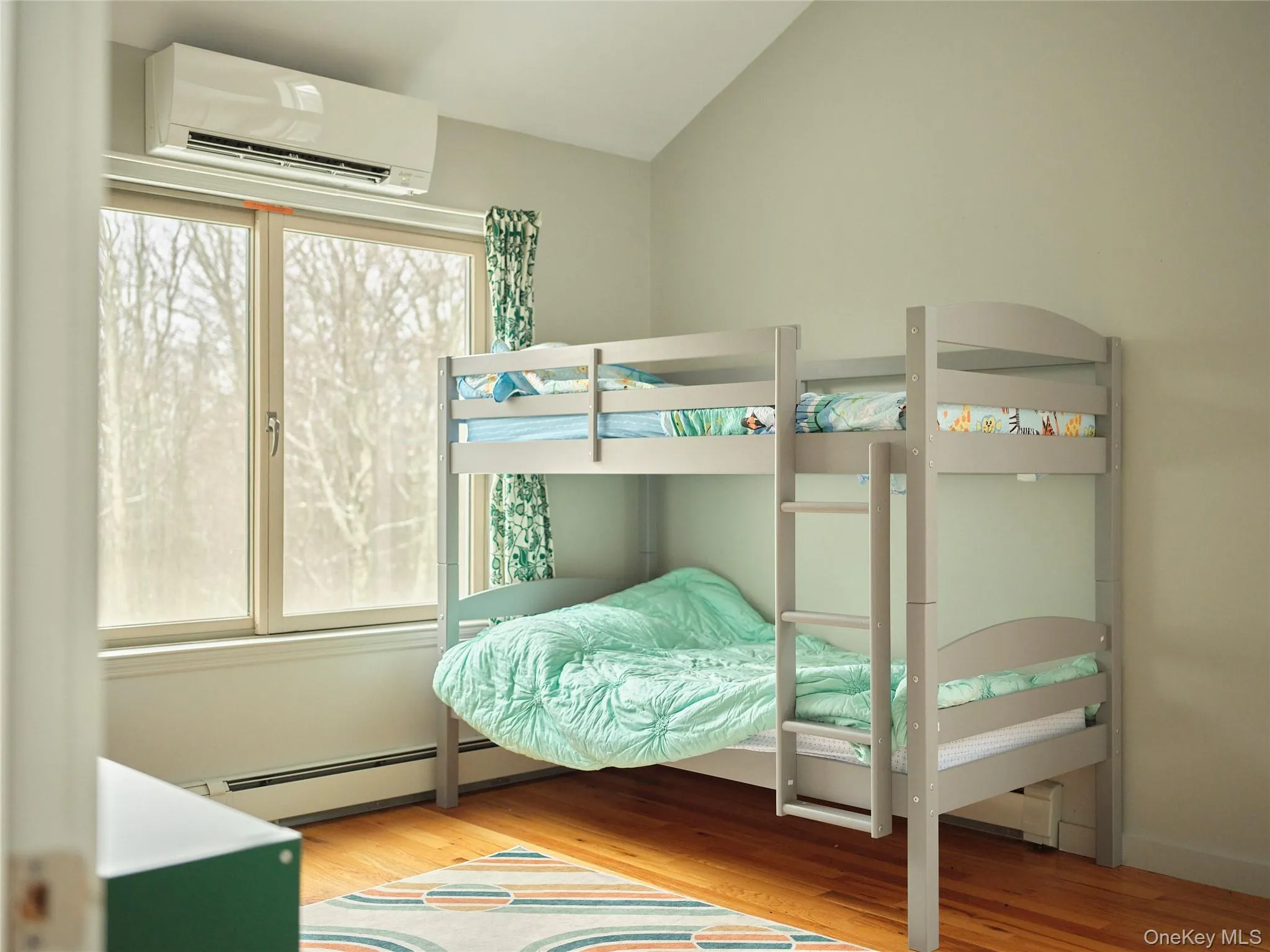 Bedroom featuring an AC wall unit, light wood-style flooring, a baseboard radiator, and lofted ceiling Bedroom featuring an AC wall unit, light wood-style flooring, a baseboard radiator, and lofted ceiling