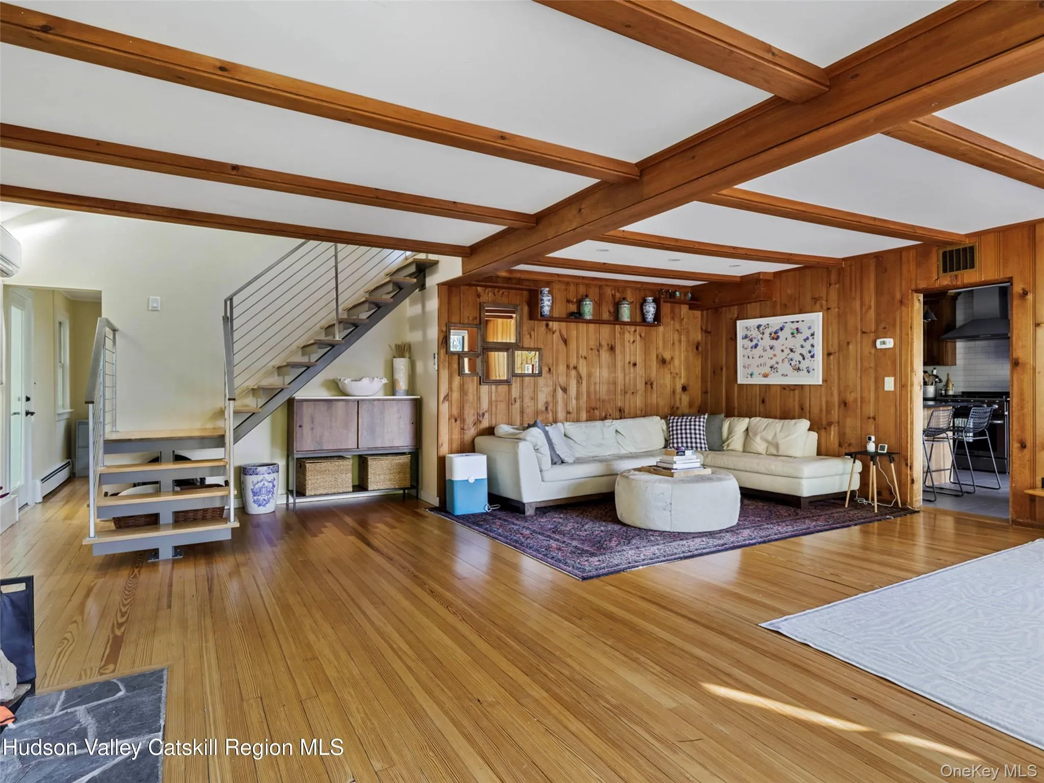 Living room with wood walls, beamed ceiling, hardwood / wood-style flooring, stairway, and a baseboard radiator Living room with wood walls, beamed ceiling, hardwood / wood-style flooring, stairway, and a baseboard radiator