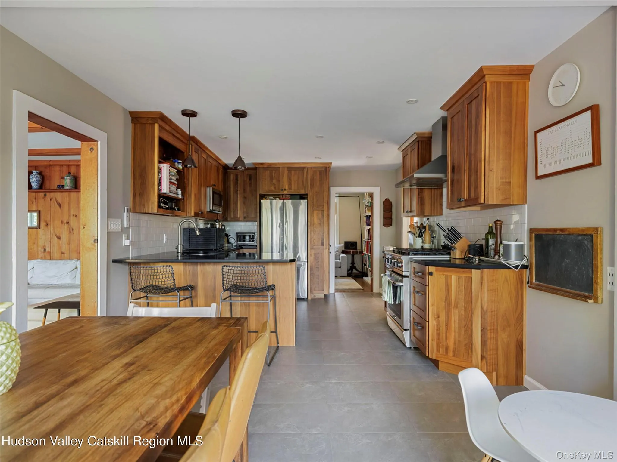 Kitchen with dark countertops, wall chimney exhaust hood, stainless steel appliances, brown cabinetry, and a peninsula Kitchen with dark countertops, wall chimney exhaust hood, stainless steel appliances, brown cabinetry, and a peninsula