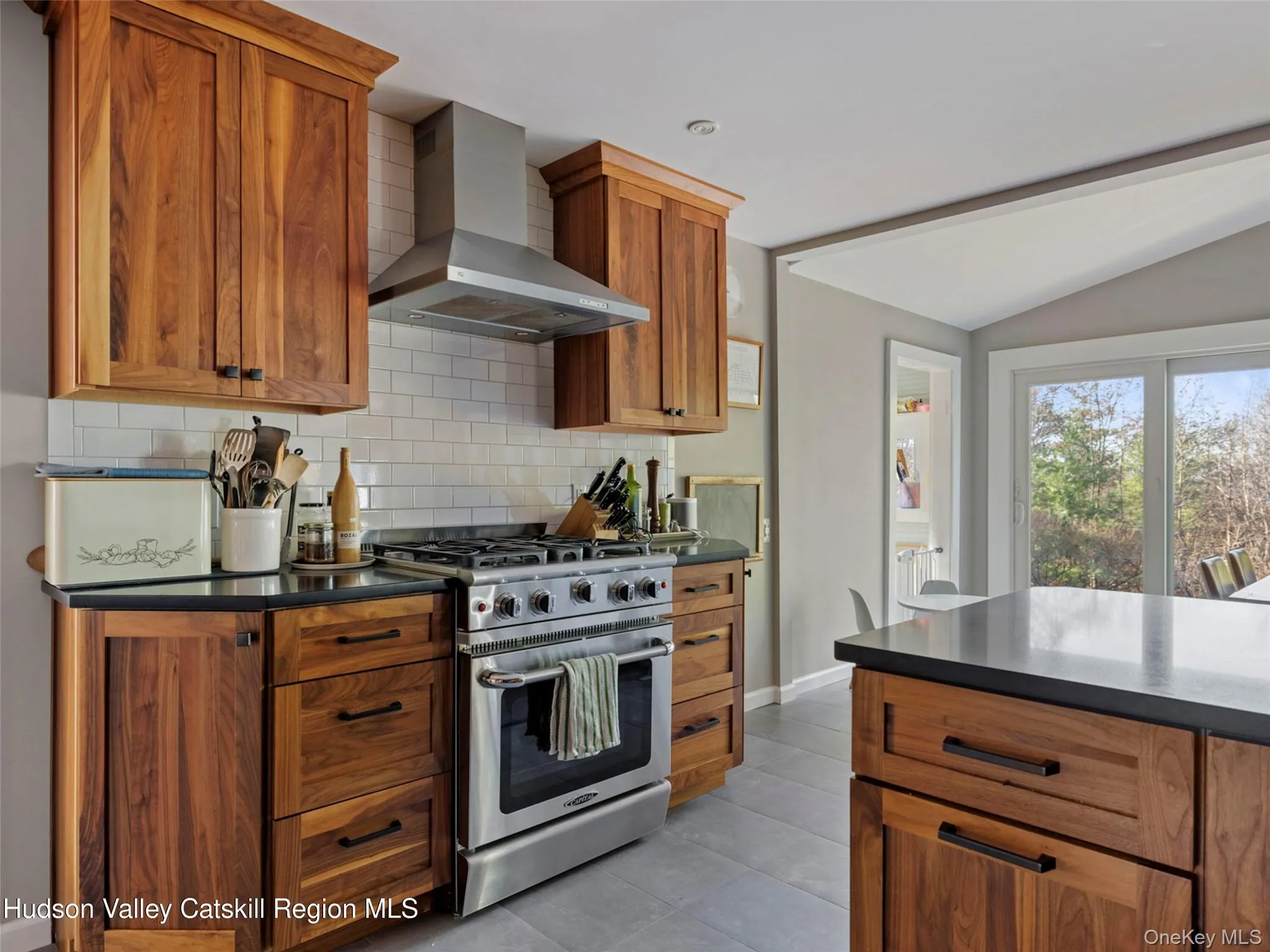 Kitchen with dark countertops, stainless steel range with gas stovetop, wall chimney range hood, lofted ceiling, and decorative backsplash Kitchen with dark countertops, stainless steel range with gas stovetop, wall chimney range hood, lofted ceiling, and decorative backsplash
