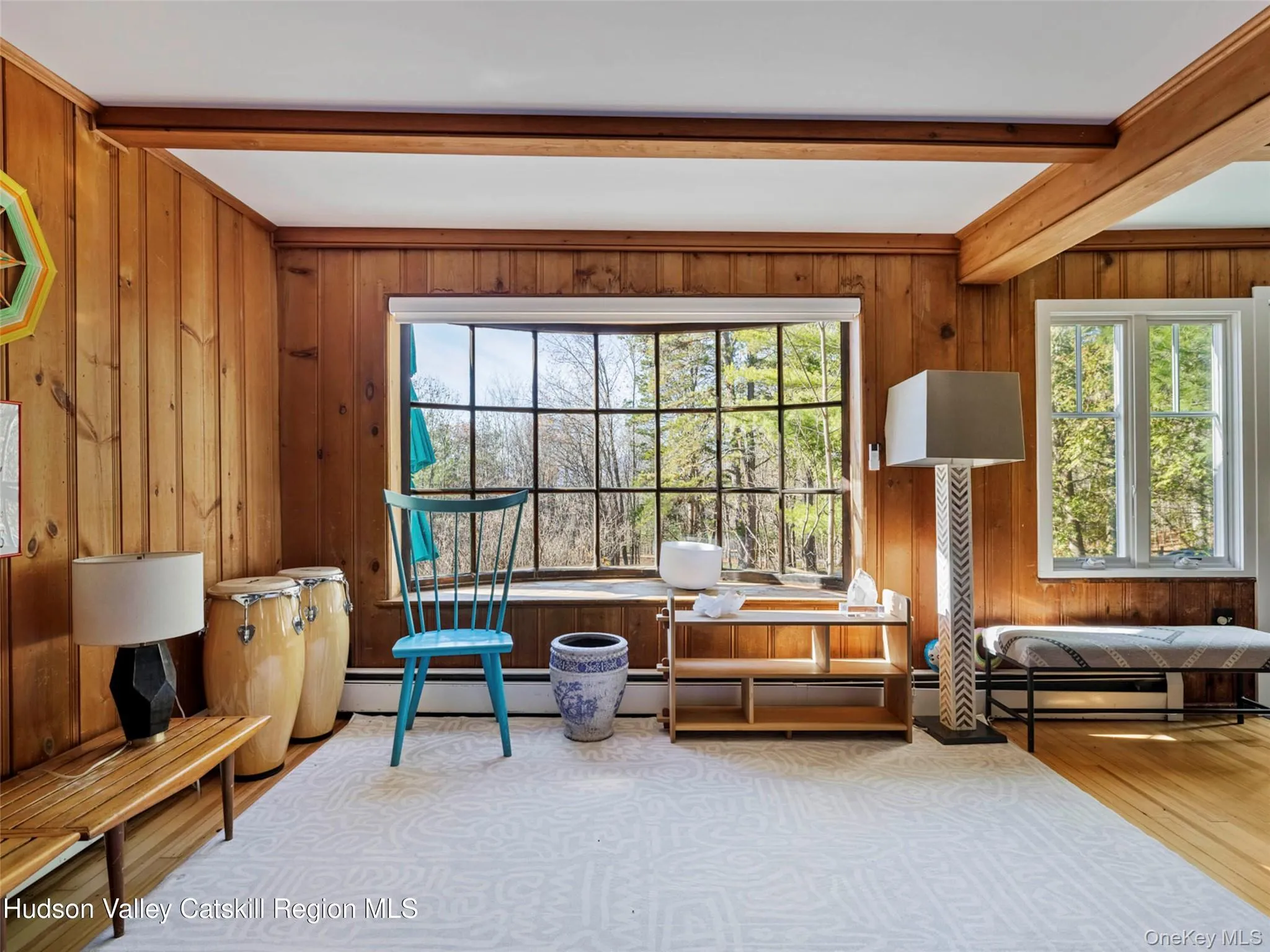 Living area featuring beamed ceiling, wood finished floors, a baseboard radiator, and wood walls Living area featuring beamed ceiling, wood finished floors, a baseboard radiator, and wood walls