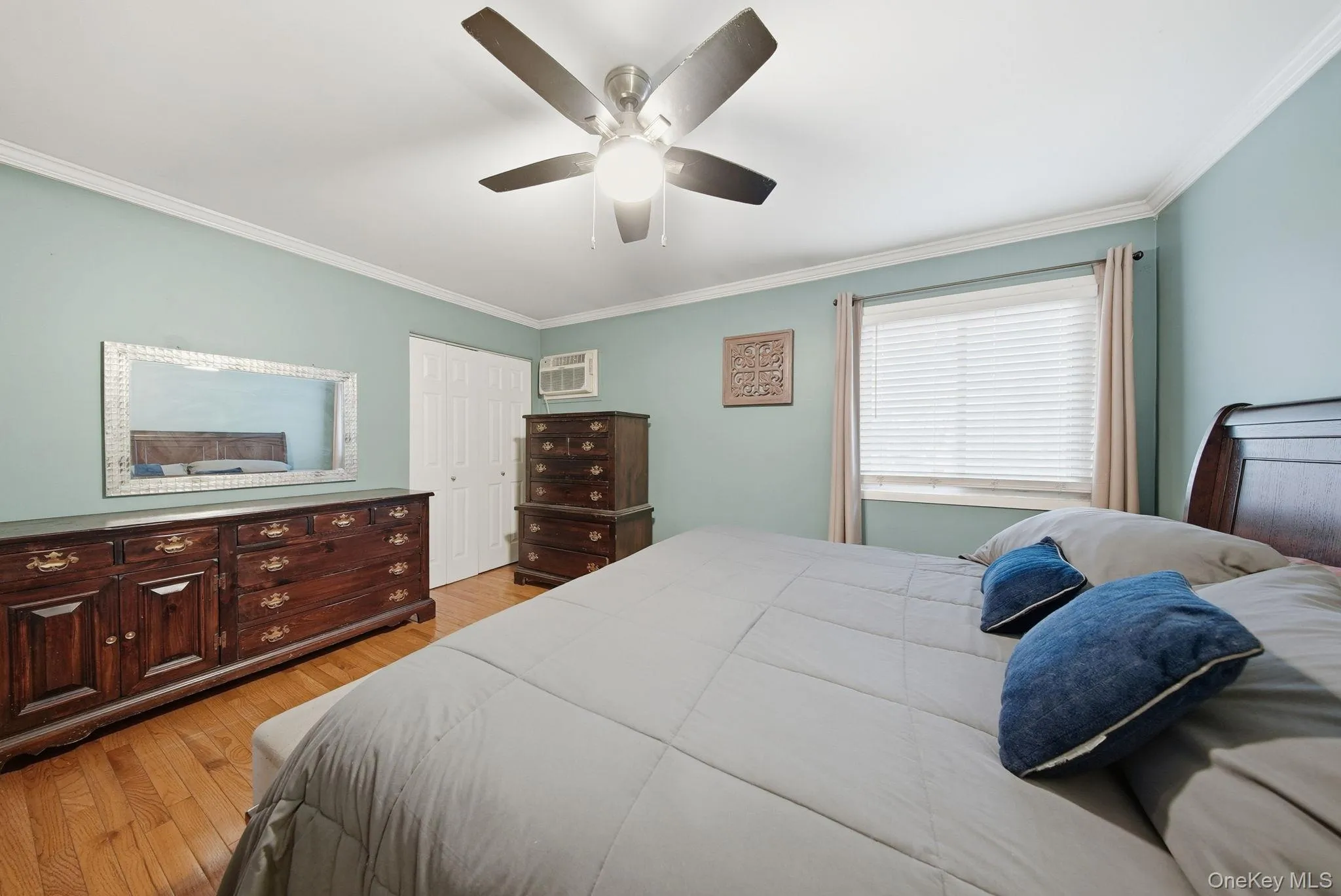 Bedroom with light wood finished floors, crown molding, ceiling fan, a closet, and a wall unit AC Bedroom with light wood finished floors, crown molding, ceiling fan, a closet, and a wall unit AC