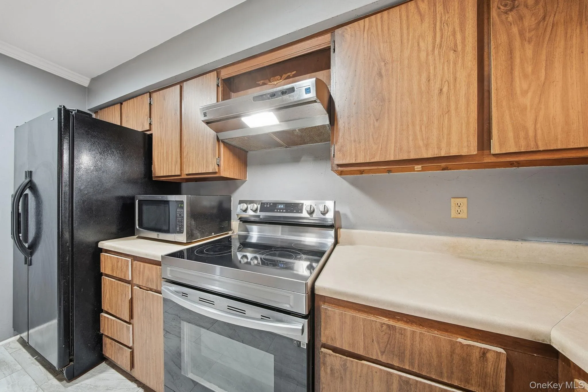 Kitchen with stainless steel appliances, under cabinet range hood, light countertops, and crown molding Kitchen with stainless steel appliances, under cabinet range hood, light countertops, and crown molding