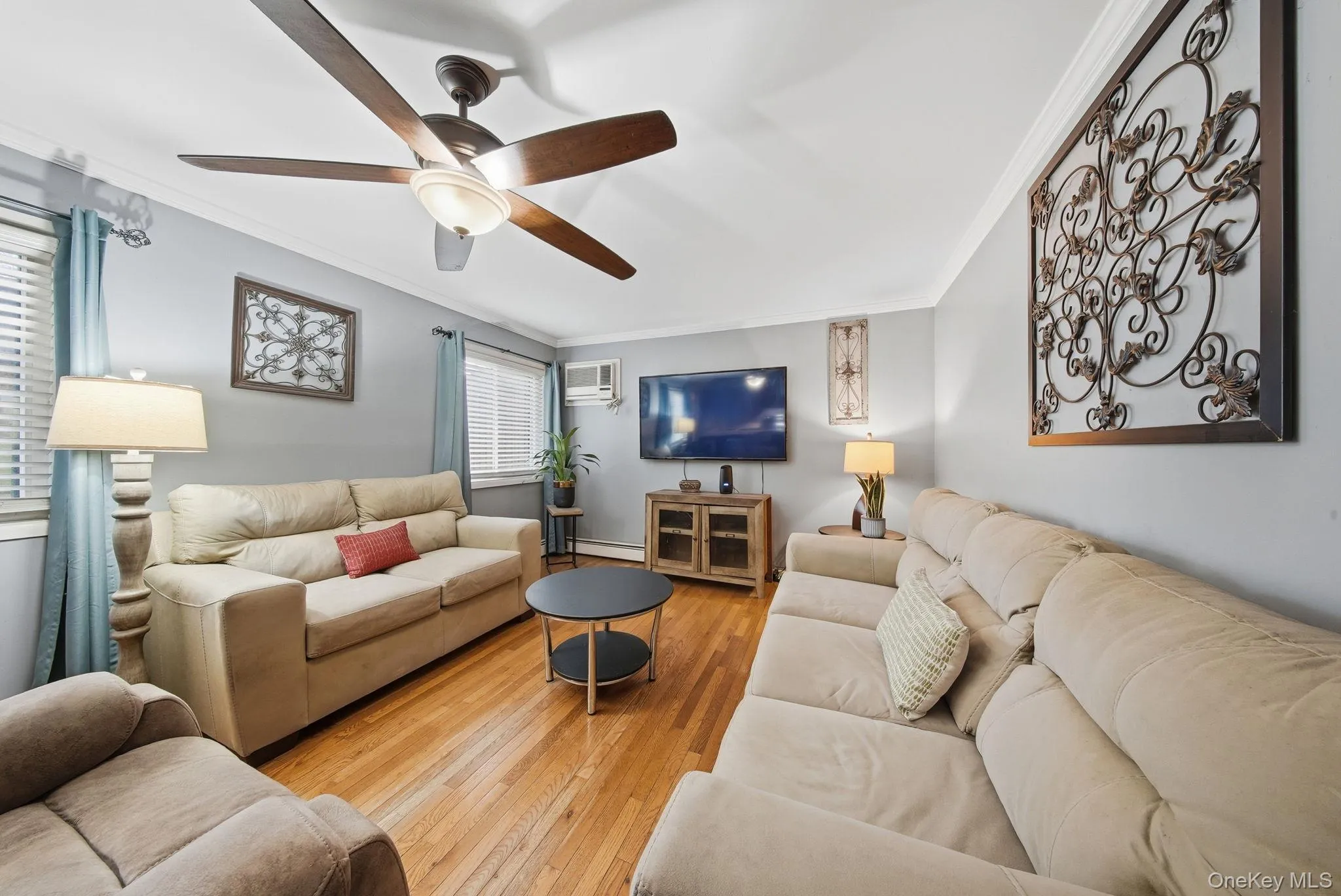 Living area featuring crown molding, hardwood / wood-style floors, a wall mounted air conditioner, ceiling fan, and a baseboard radiator Living area featuring crown molding, hardwood / wood-style floors, a wall mounted air conditioner, ceiling fan, and a baseboard radiator