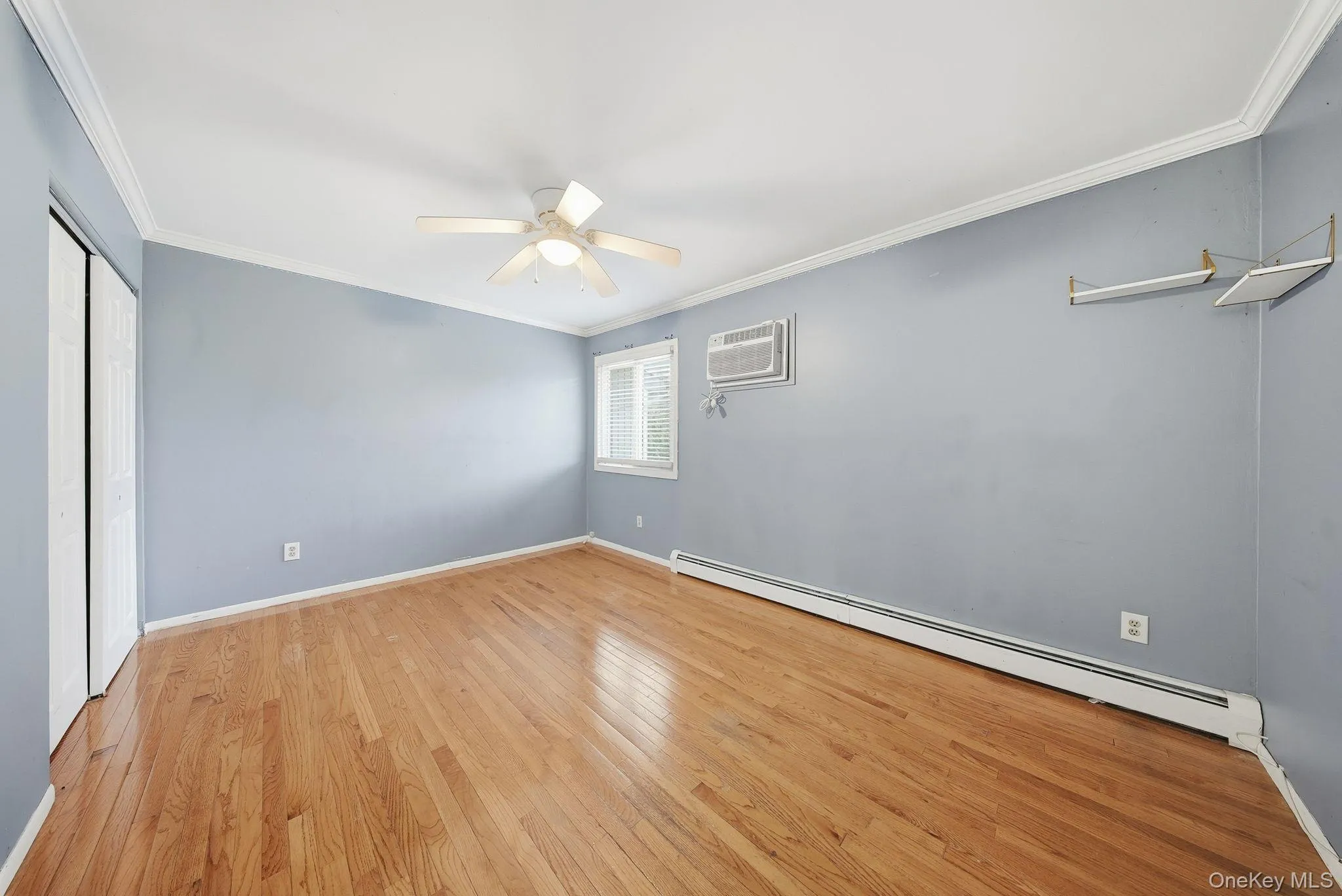 Unfurnished bedroom featuring a baseboard heating unit, crown molding, light wood-style floors, a ceiling fan, and a closet Unfurnished bedroom featuring a baseboard heating unit, crown molding, light wood-style floors, a ceiling fan, and a closet