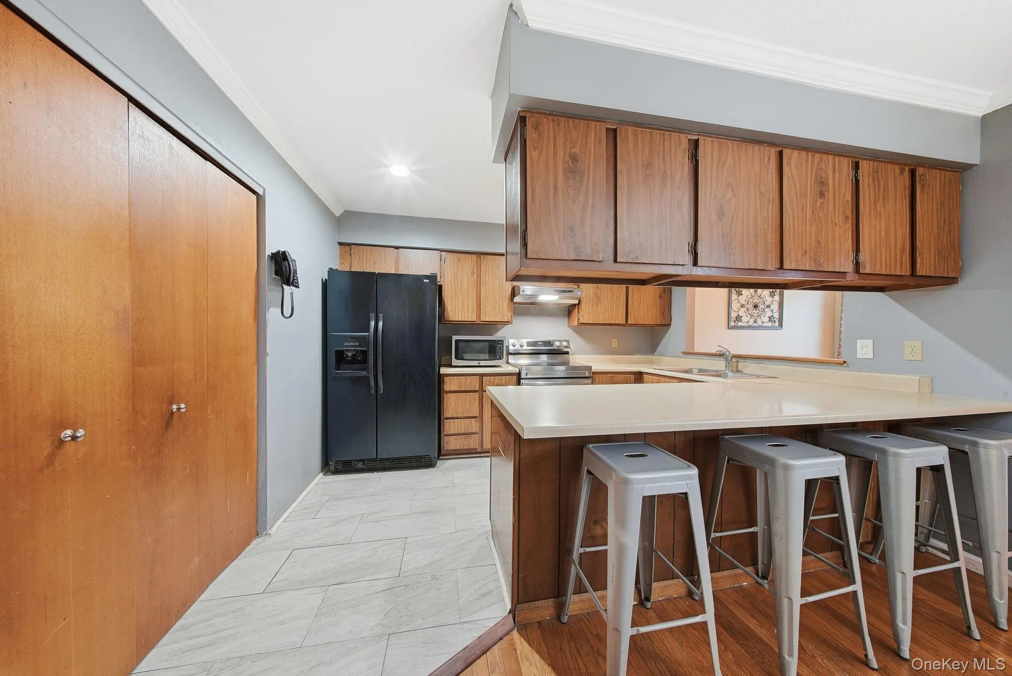 Kitchen with light countertops, stainless steel appliances, ornamental molding, a peninsula, and a kitchen bar Kitchen with light countertops, stainless steel appliances, ornamental molding, a peninsula, and a kitchen bar