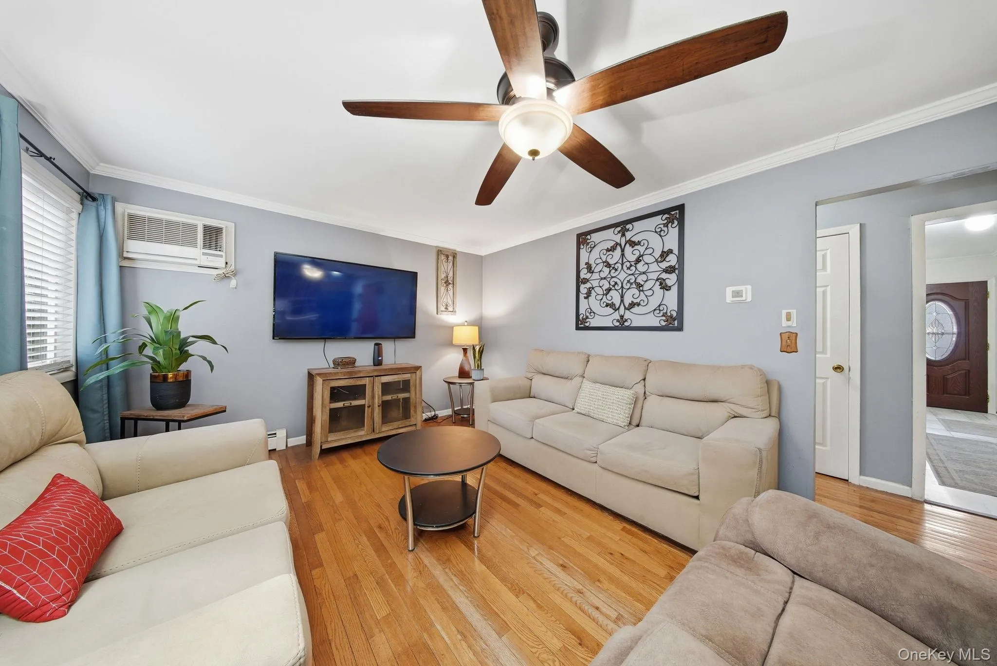 Living area with hardwood / wood-style flooring, crown molding, a ceiling fan, and a wall unit AC Living area with hardwood / wood-style flooring, crown molding, a ceiling fan, and a wall unit AC