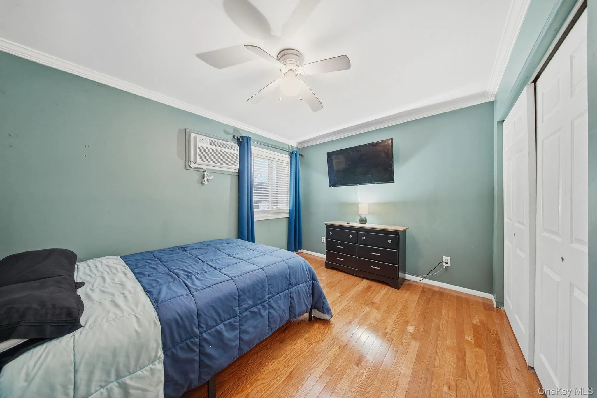 Bedroom featuring ornamental molding, a closet, wood-type flooring, a ceiling fan, and a wall mounted AC Bedroom featuring ornamental molding, a closet, wood-type flooring, a ceiling fan, and a wall mounted AC