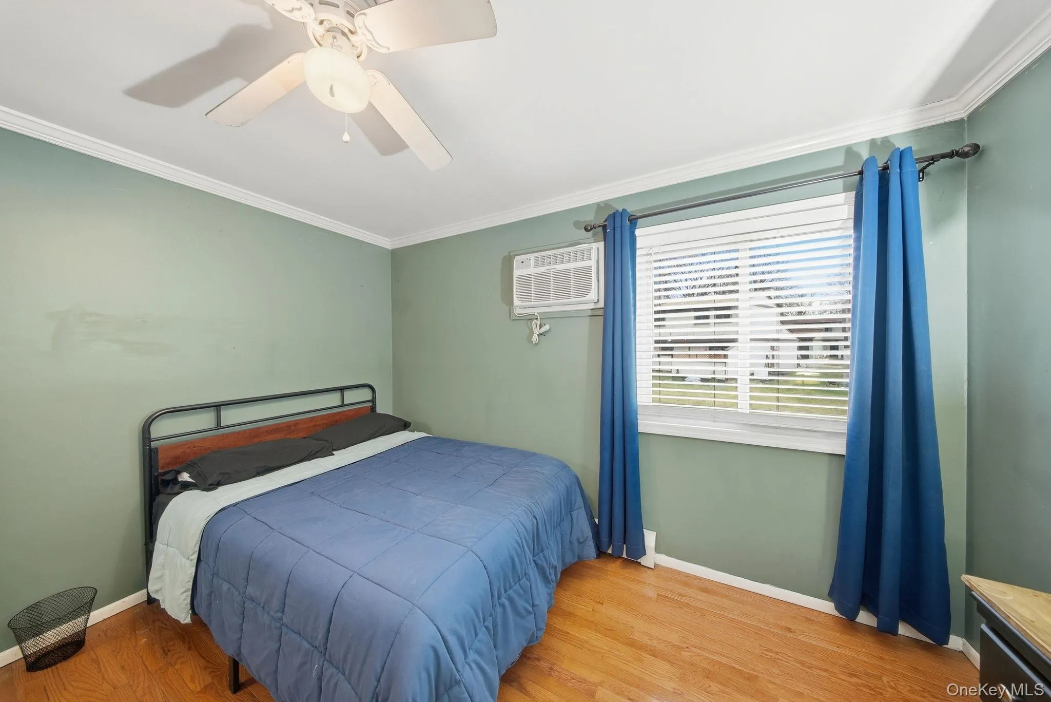 Bedroom with wood finished floors, a ceiling fan, crown molding, and a wall mounted air conditioner Bedroom with wood finished floors, a ceiling fan, crown molding, and a wall mounted air conditioner
