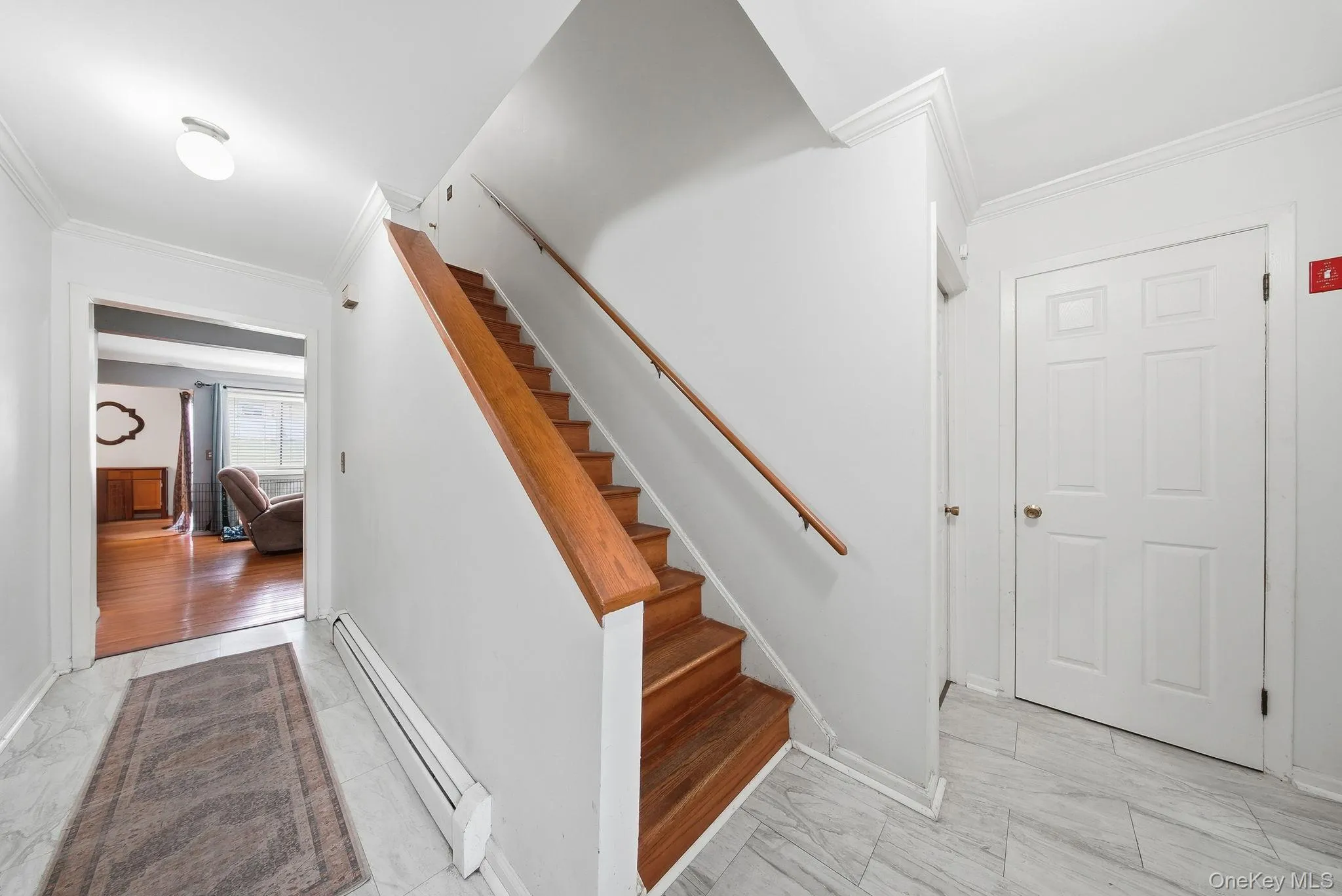 Stairs featuring ornamental molding, a baseboard radiator, and marble look tiles Stairs featuring ornamental molding, a baseboard radiator, and marble look tiles