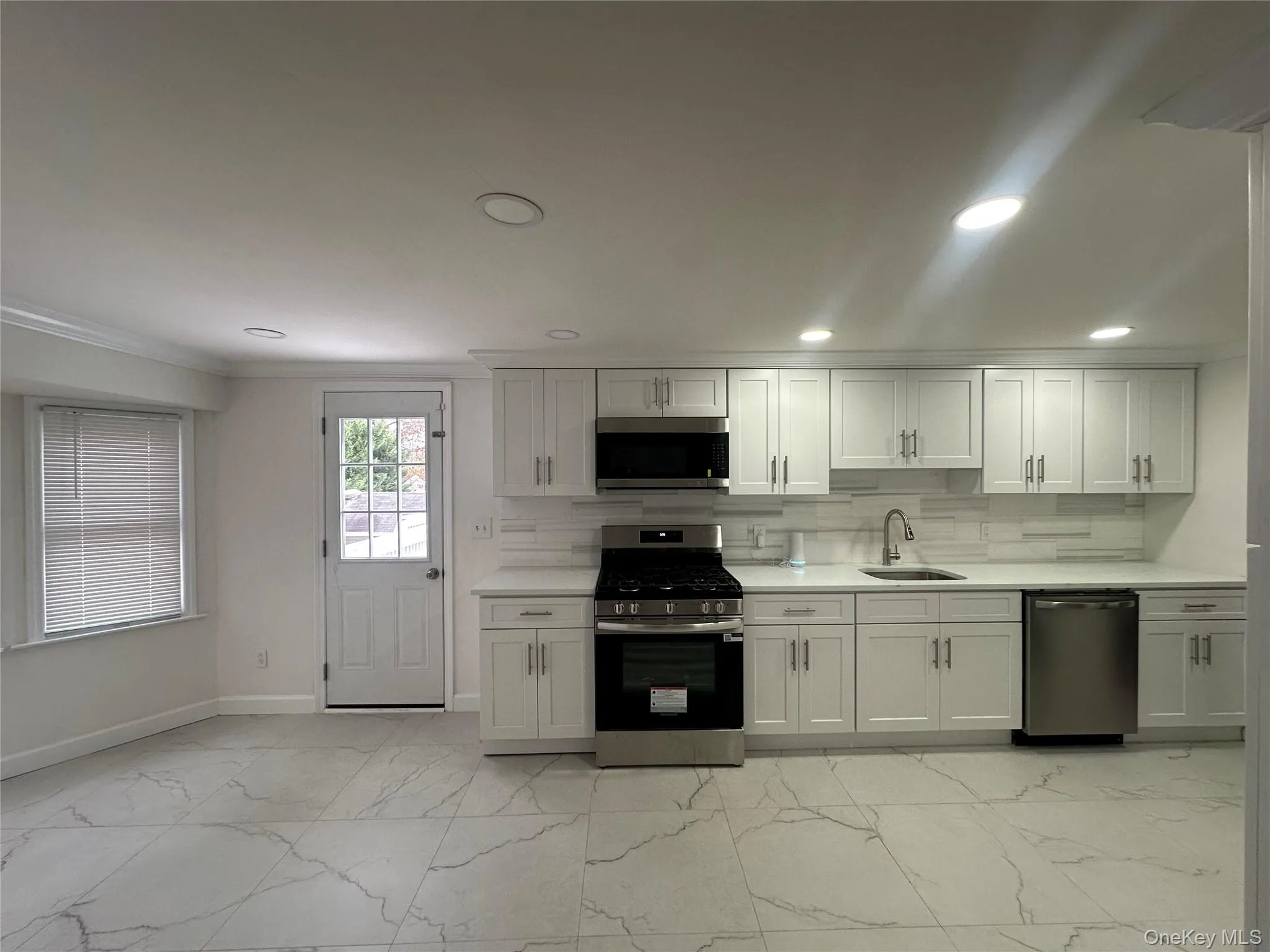 Kitchen with stainless steel appliances, light marble finish floors, white cabinetry, crown molding, and light stone countertops Kitchen with stainless steel appliances, light marble finish floors, white cabinetry, crown molding, and light stone countertops