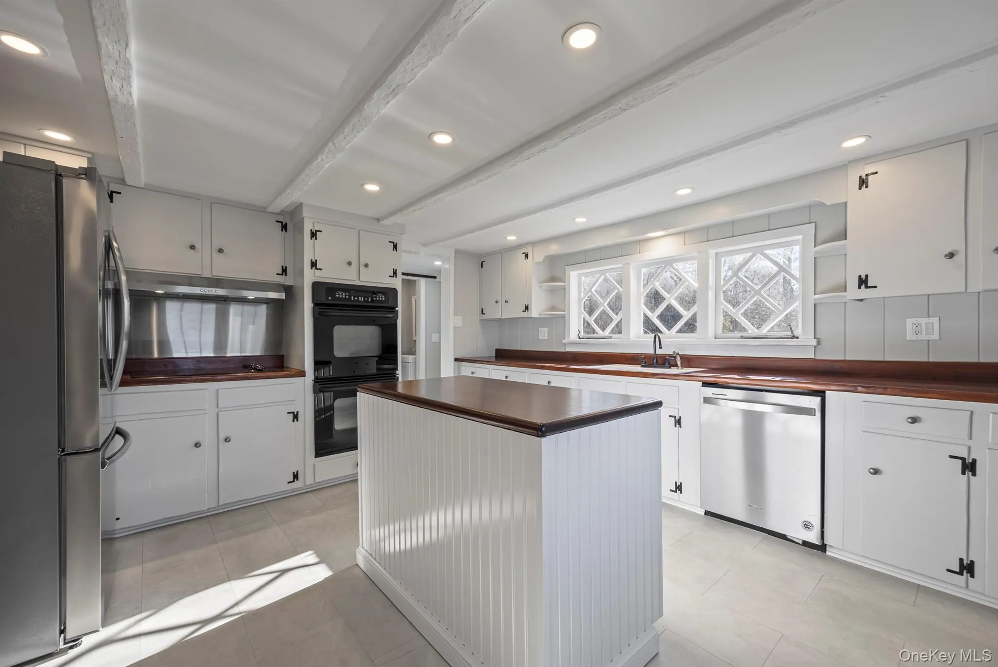 Kitchen with open shelves, stainless steel appliances, beam ceiling, white cabinetry, and recessed lighting Kitchen with open shelves, stainless steel appliances, beam ceiling, white cabinetry, and recessed lighting