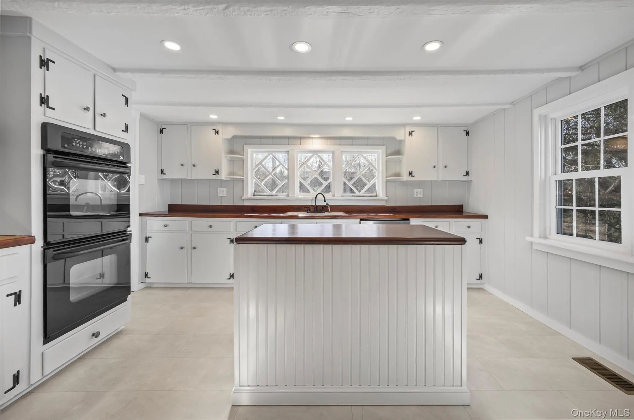 Kitchen with open shelves, white cabinets, beam ceiling, wood walls, and recessed lighting Kitchen with open shelves, white cabinets, beam ceiling, wood walls, and recessed lighting