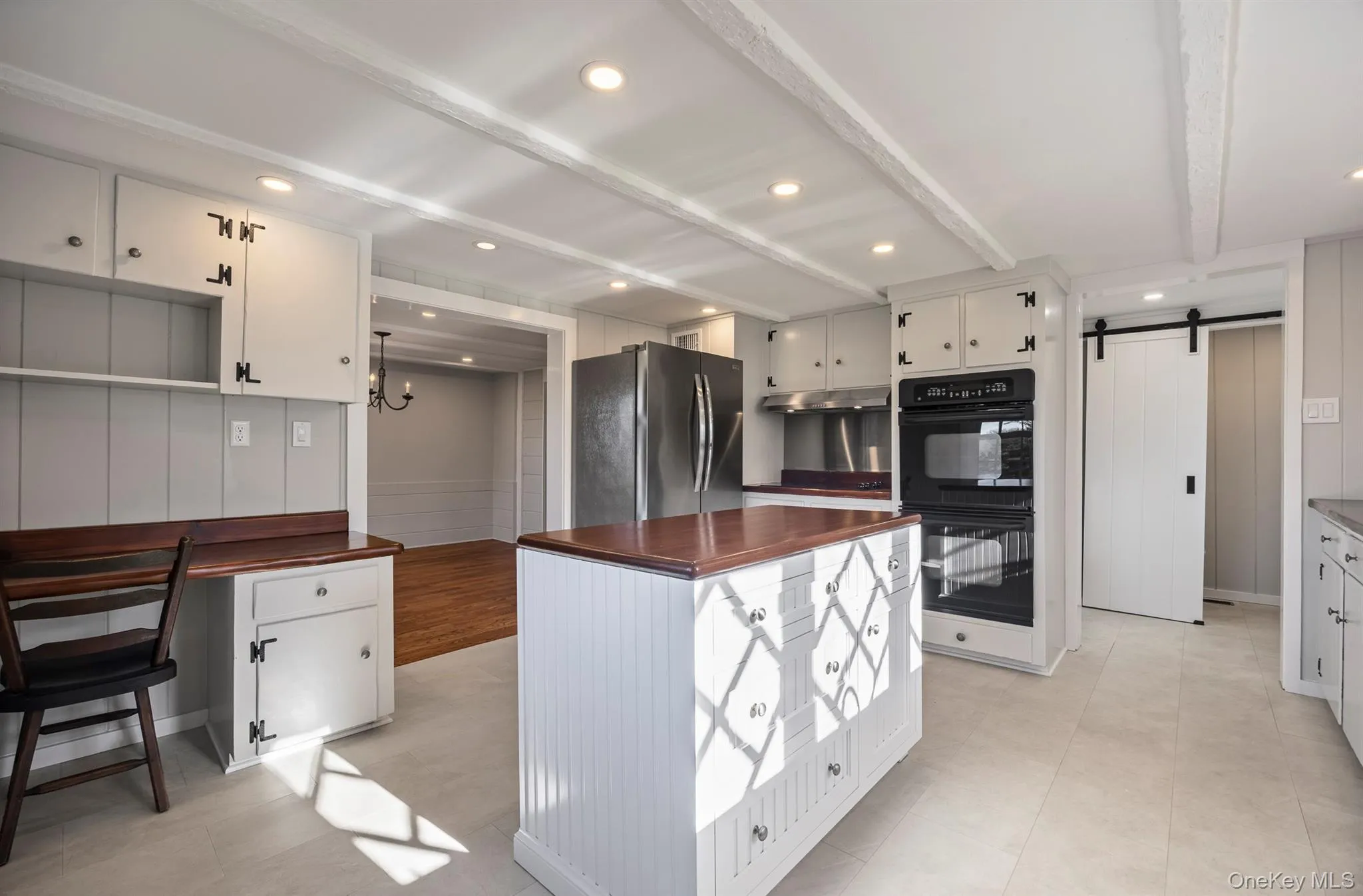 Kitchen with beamed ceiling, freestanding refrigerator, a barn door, white cabinets, and a center island Kitchen with beamed ceiling, freestanding refrigerator, a barn door, white cabinets, and a center island