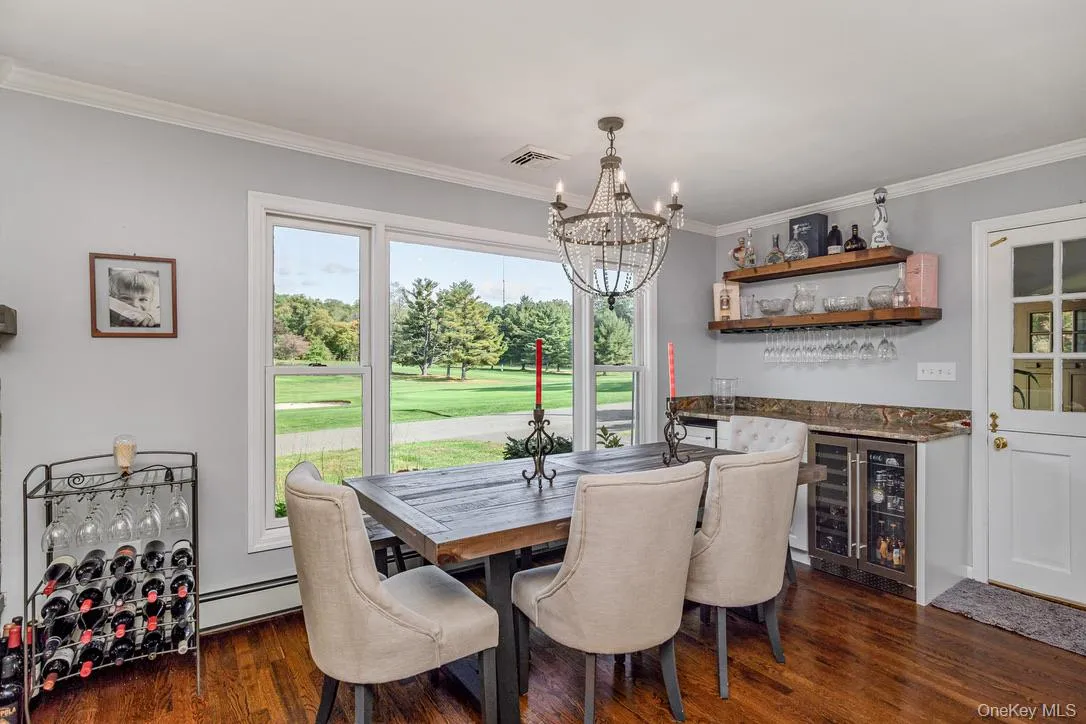 Dining room featuring wine cooler, ornamental molding, a chandelier, a baseboard radiator, and dark wood-style flooring Dining room featuring wine cooler, ornamental molding, a chandelier, a baseboard radiator, and dark wood-style flooring