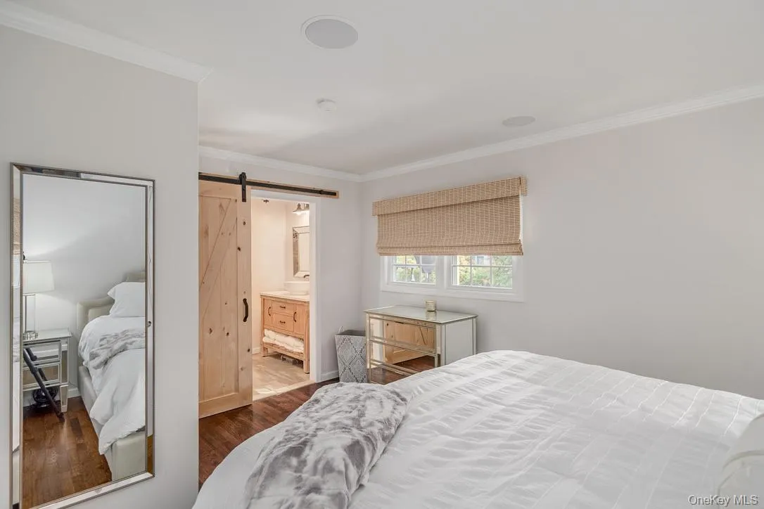 Bedroom featuring a barn door, ornamental molding, dark wood-style flooring, and ensuite bath Bedroom featuring a barn door, ornamental molding, dark wood-style flooring, and ensuite bath