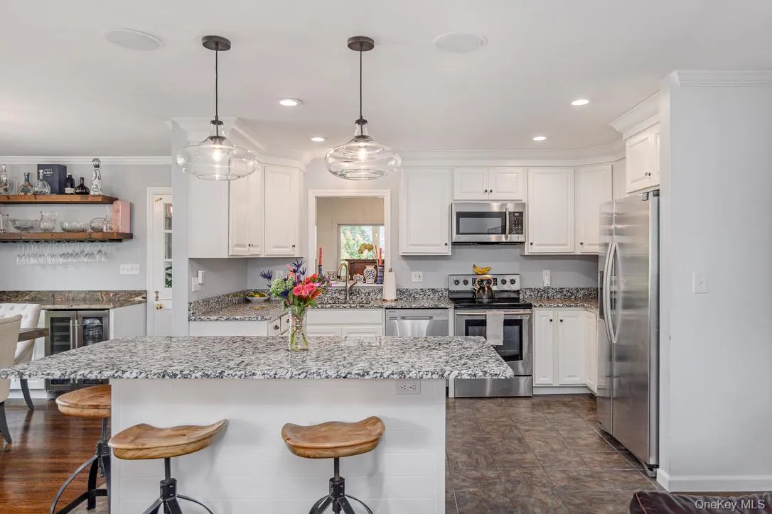 Kitchen featuring stainless steel appliances, a breakfast bar, white cabinetry, decorative light fixtures, and ornamental molding Kitchen featuring stainless steel appliances, a breakfast bar, white cabinetry, decorative light fixtures, and ornamental molding