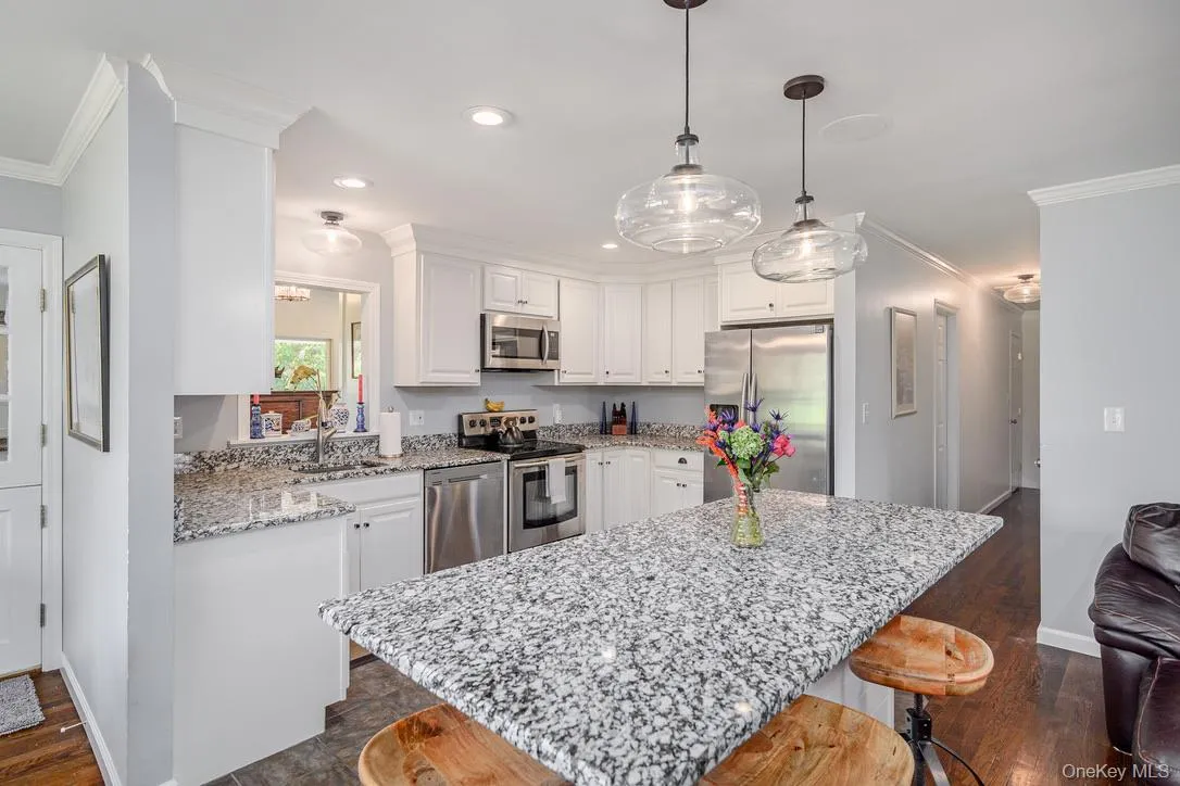 Kitchen featuring crown molding, a kitchen bar, appliances with stainless steel finishes, white cabinets, and light stone countertops Kitchen featuring crown molding, a kitchen bar, appliances with stainless steel finishes, white cabinets, and light stone countertops