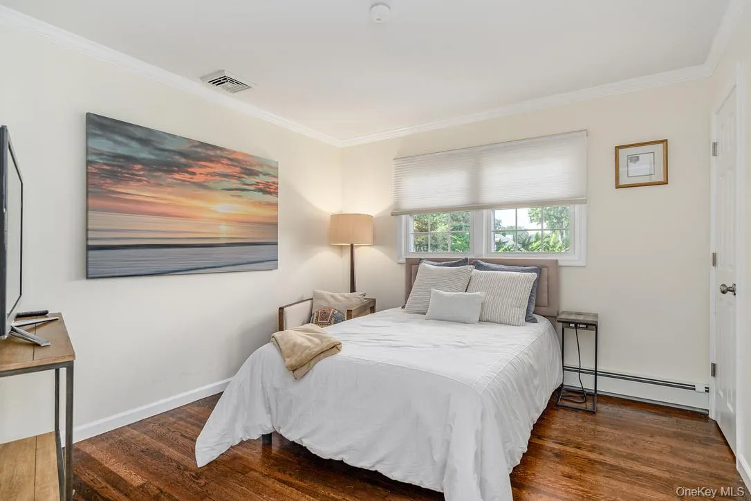 Bedroom featuring baseboard heating, dark wood-type flooring, and ornamental molding Bedroom featuring baseboard heating, dark wood-type flooring, and ornamental molding