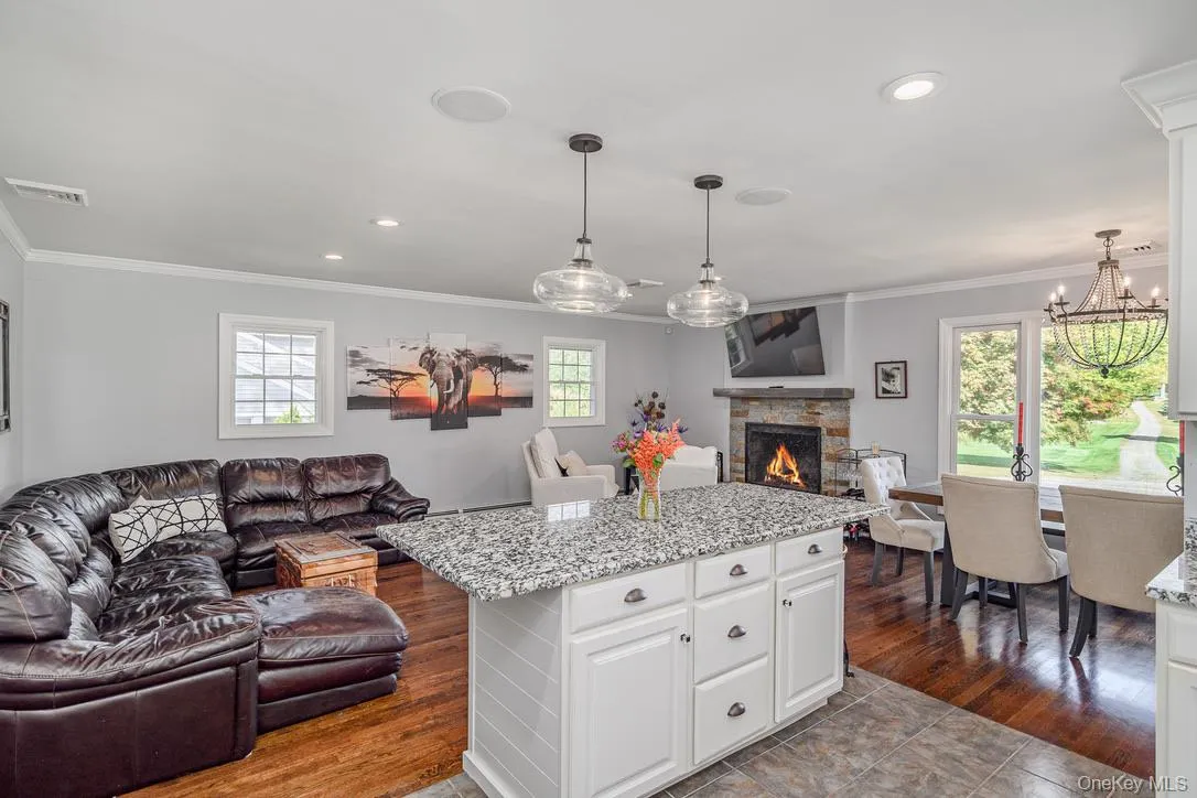 Kitchen with open floor plan, light stone counters, white cabinetry, a fireplace, and ornamental molding Kitchen with open floor plan, light stone counters, white cabinetry, a fireplace, and ornamental molding