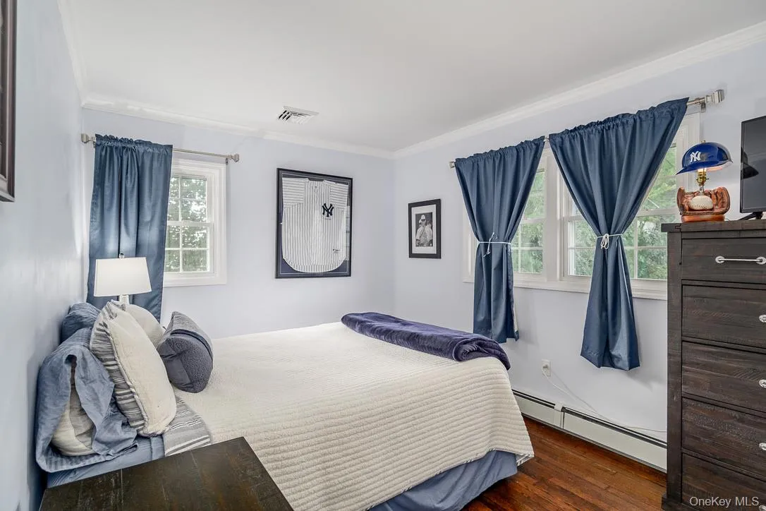 Bedroom featuring a baseboard heating unit, dark wood-style floors, and crown molding Bedroom featuring a baseboard heating unit, dark wood-style floors, and crown molding
