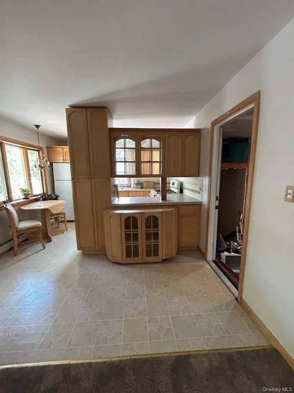 Kitchen featuring freestanding refrigerator, glass insert cabinets, hanging light fixtures, a chandelier, and light countertops Kitchen featuring freestanding refrigerator, glass insert cabinets, hanging light fixtures, a chandelier, and light countertops