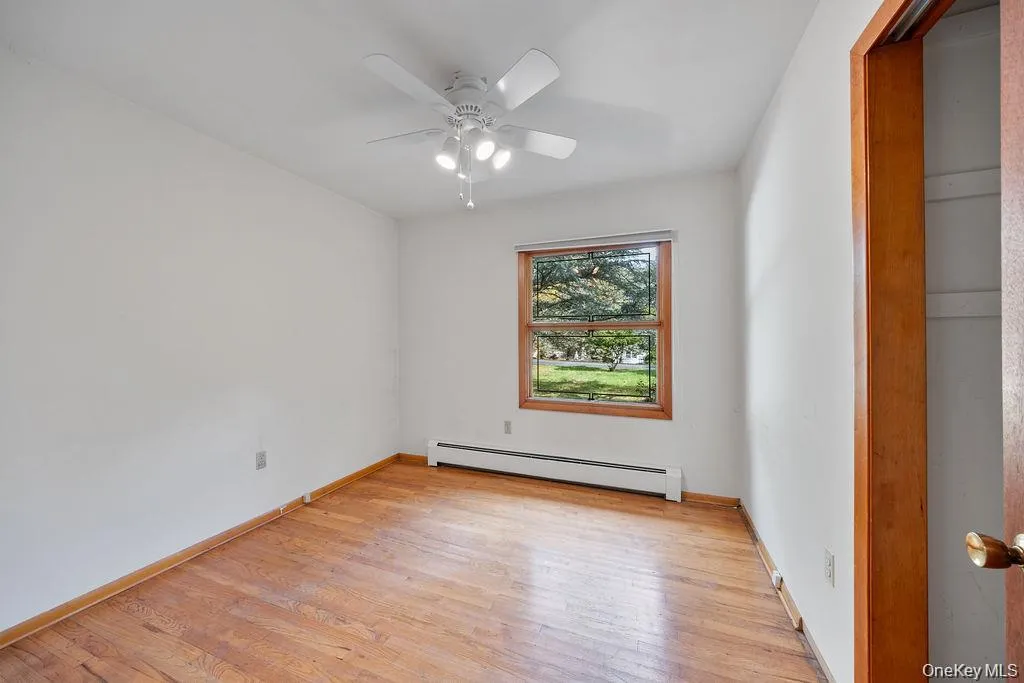 Unfurnished room with a baseboard heating unit, light wood-style flooring, and ceiling fan Unfurnished room with a baseboard heating unit, light wood-style flooring, and ceiling fan