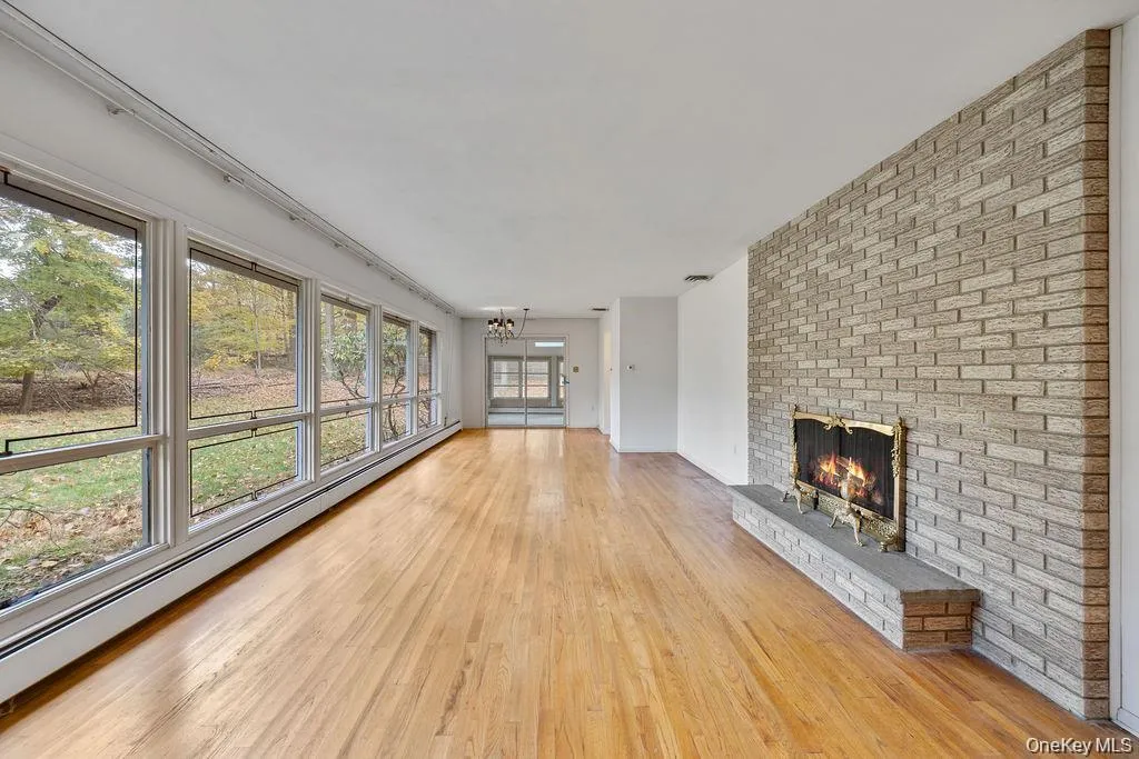 Unfurnished living room with baseboard heating, a fireplace, light wood-style floors, and a chandelier Unfurnished living room with baseboard heating, a fireplace, light wood-style floors, and a chandelier