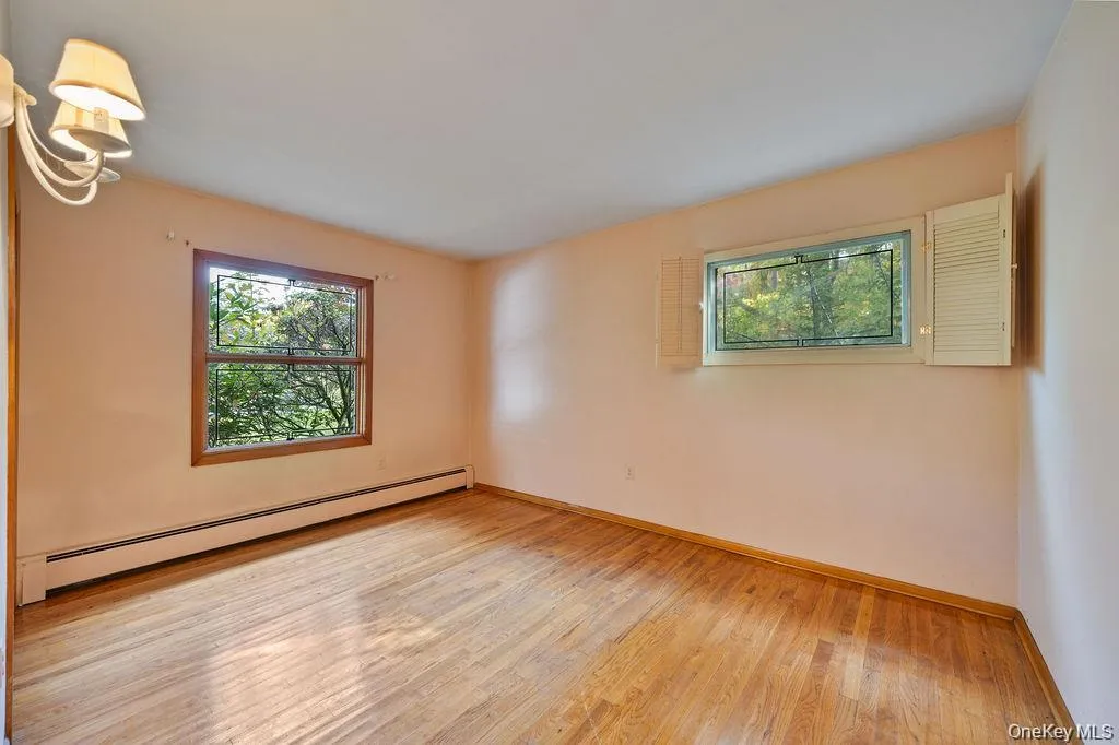 Empty room with baseboard heating, light wood-style flooring, and healthy amount of natural light Empty room with baseboard heating, light wood-style flooring, and healthy amount of natural light