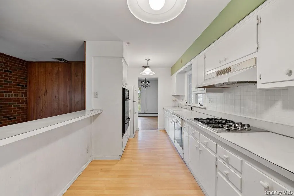 Kitchen with light countertops, white cabinets, light wood-style floors, hanging light fixtures, and brick wall Kitchen with light countertops, white cabinets, light wood-style floors, hanging light fixtures, and brick wall