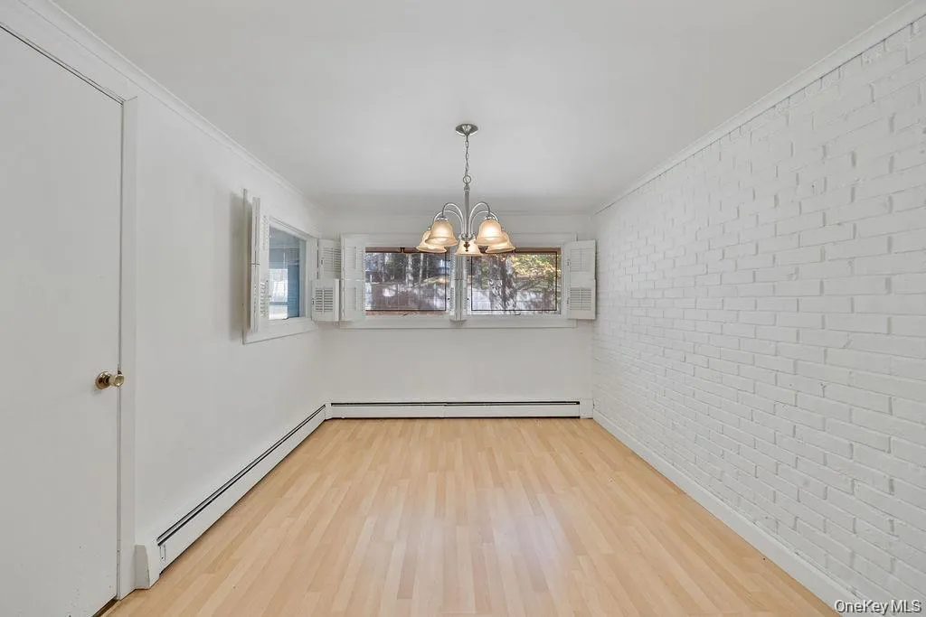 Unfurnished dining area with a baseboard radiator, ornamental molding, brick wall, a chandelier, and wood finished floors Unfurnished dining area with a baseboard radiator, ornamental molding, brick wall, a chandelier, and wood finished floors