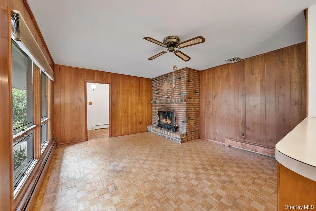 Unfurnished living room with a baseboard radiator, ceiling fan, a fireplace, and wood walls Unfurnished living room with a baseboard radiator, ceiling fan, a fireplace, and wood walls