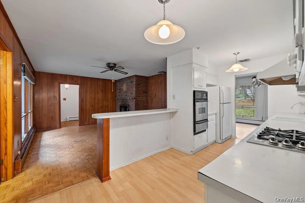 Kitchen with decorative light fixtures, light countertops, white cabinetry, a baseboard radiator, and wood walls Kitchen with decorative light fixtures, light countertops, white cabinetry, a baseboard radiator, and wood walls