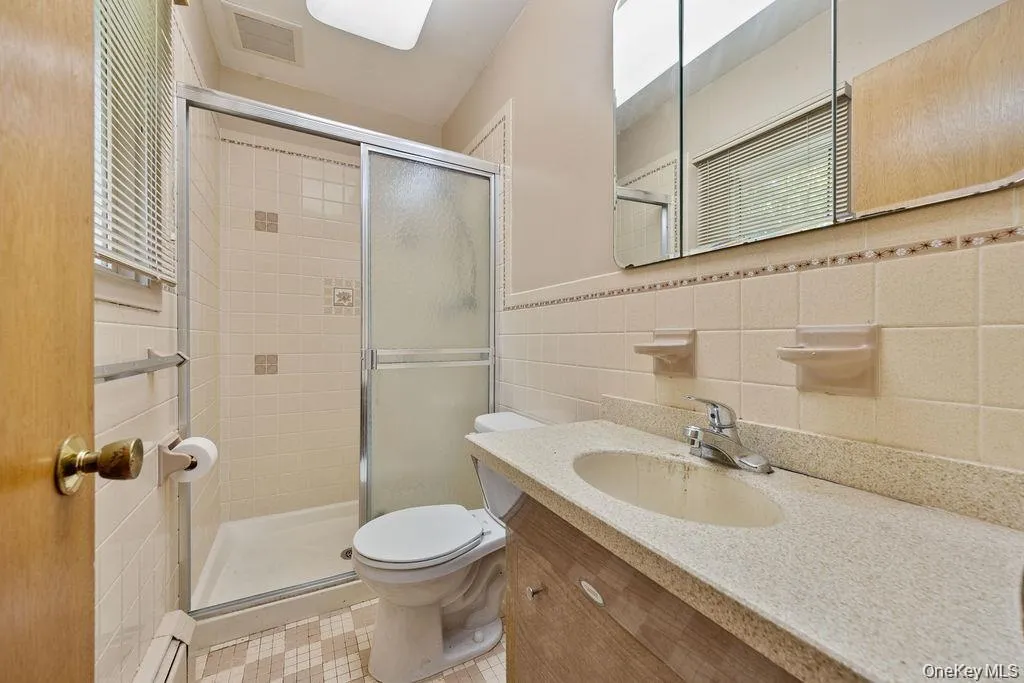 Bathroom featuring tile walls, vanity, a shower stall, a baseboard radiator, and a wainscoted wall Bathroom featuring tile walls, vanity, a shower stall, a baseboard radiator, and a wainscoted wall