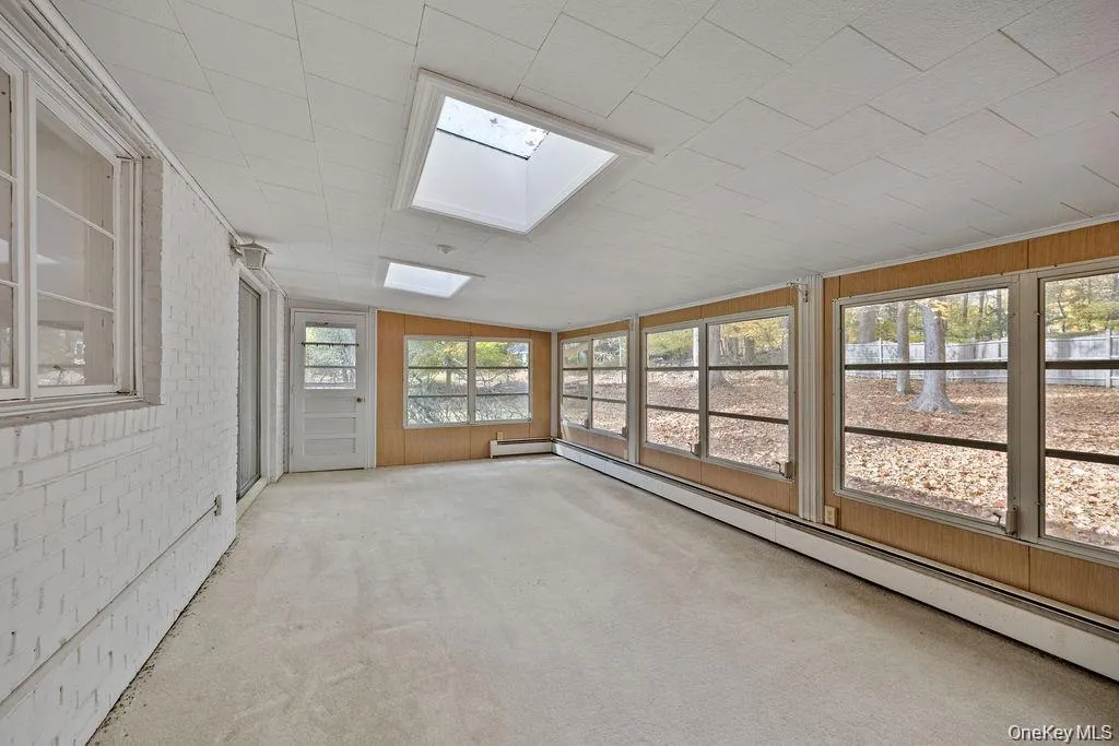 Unfurnished sunroom featuring a skylight, a baseboard heating unit, brick wall, and carpet Unfurnished sunroom featuring a skylight, a baseboard heating unit, brick wall, and carpet