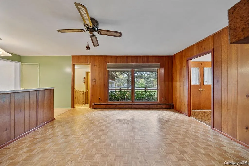 Unfurnished living room featuring wood walls, baseboard heating, light floors, and ceiling fan Unfurnished living room featuring wood walls, baseboard heating, light floors, and ceiling fan