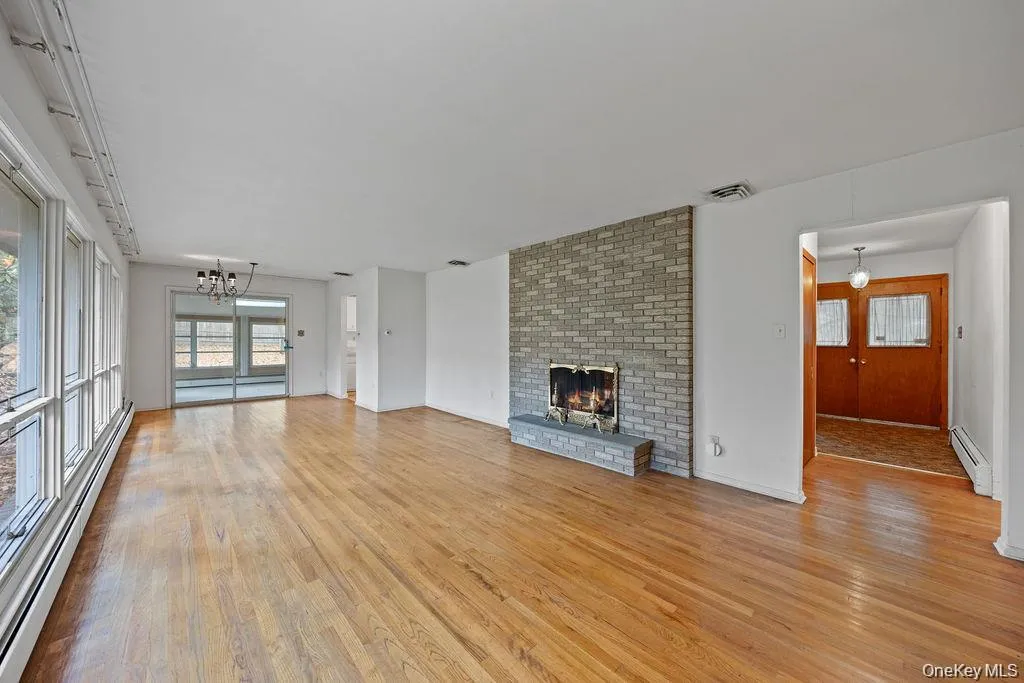 Unfurnished living room featuring a baseboard heating unit, a fireplace, a chandelier, and light wood-style flooring Unfurnished living room featuring a baseboard heating unit, a fireplace, a chandelier, and light wood-style flooring
