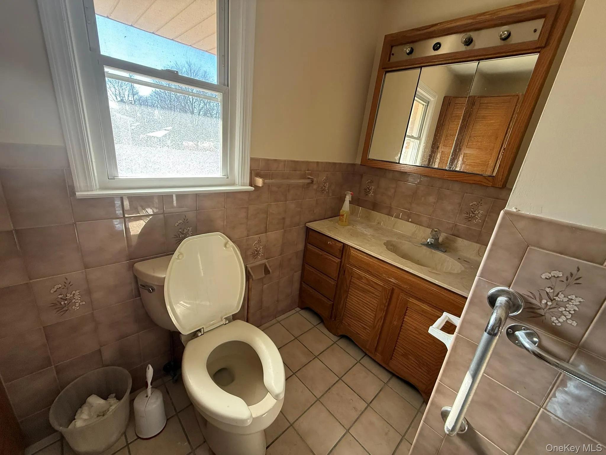 Bathroom featuring vanity, wainscoting, light tile patterned flooring, healthy amount of natural light, and tile walls Bathroom featuring vanity, wainscoting, light tile patterned flooring, healthy amount of natural light, and tile walls