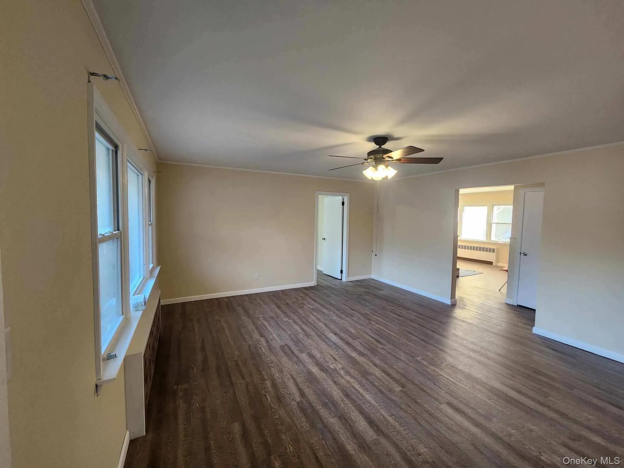 Unfurnished room featuring dark wood-style floors, radiator, crown molding, and a ceiling fan Unfurnished room featuring dark wood-style floors, radiator, crown molding, and a ceiling fan